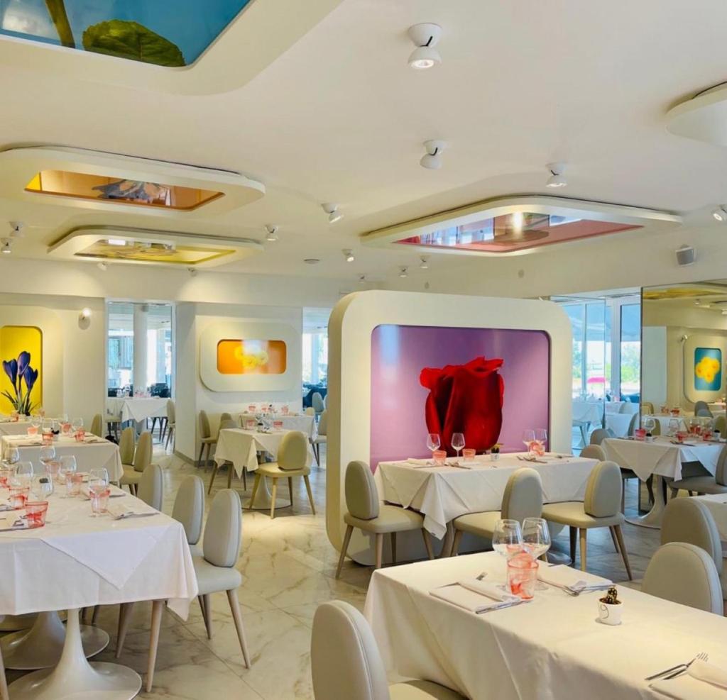 un restaurant avec des tables et des chaises blanches et un grand miroir dans l'établissement Marina Suites & Apartments 4 stelle S, à Caorle