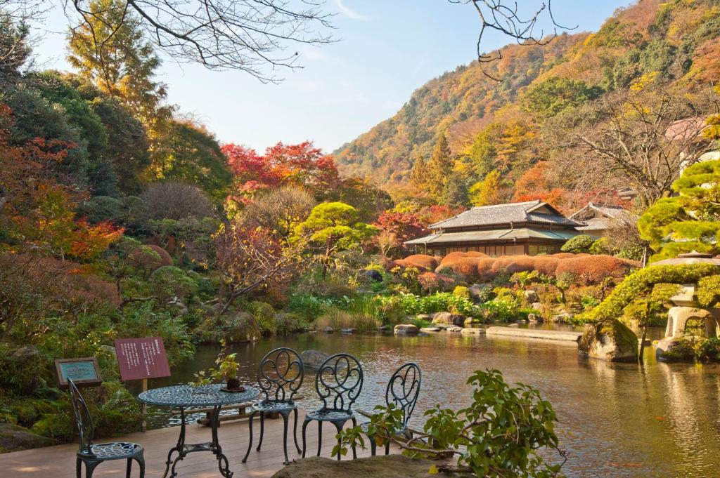 une table et des chaises dans un jardin avec une rivière dans l'établissement Yoshiike Ryokan, à Hakone