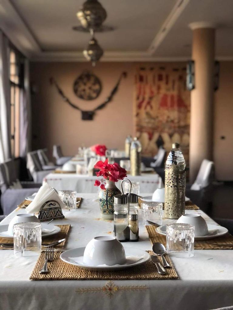 - une grande table avec des assiettes blanches et des fleurs rouges dans l'établissement Riad Tama & spa, à Ouarzazate
