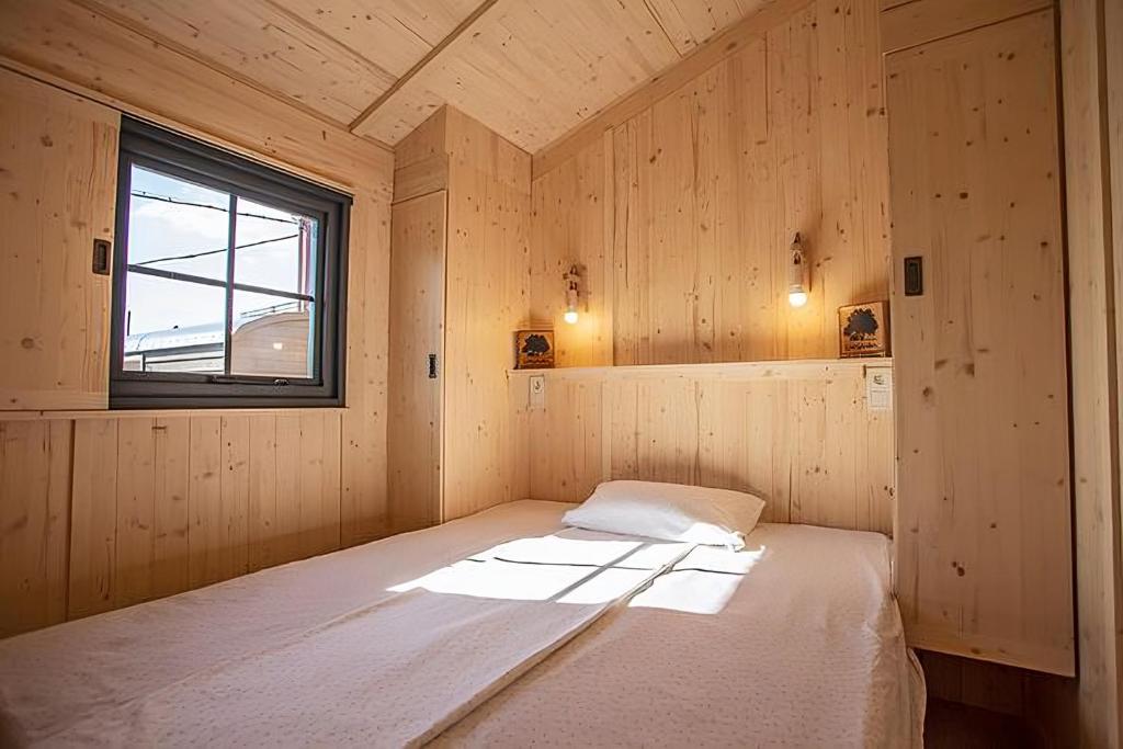 - une chambre avec un lit dans une pièce en bois dotée d'une fenêtre dans l'établissement Camping Le Gallo Romain, à Barbières