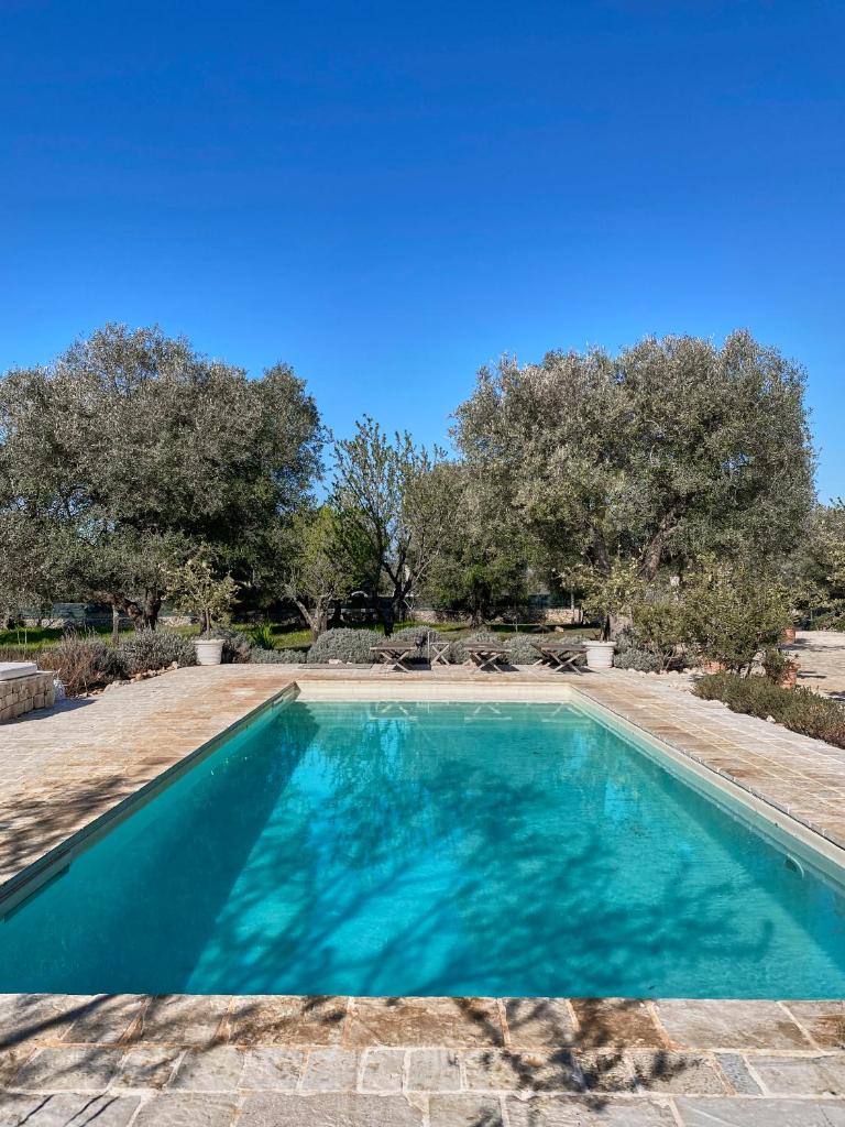 une piscine bleue avec des arbres en arrière-plan dans l'établissement TRULLO SILENTIO, Ostuni - w private pool, à Ostuni