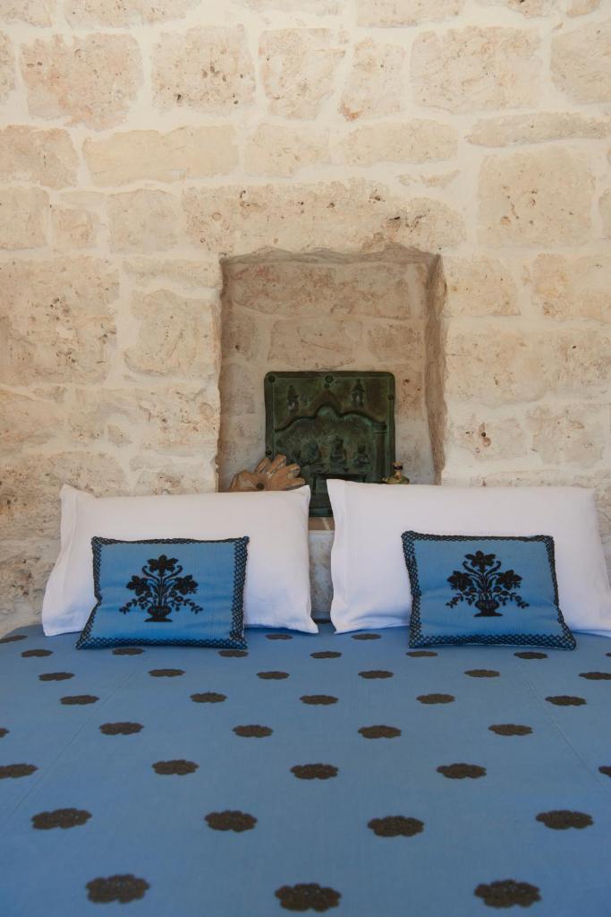 - 2 oreillers bleus et blancs sur un lit avec un mur en pierre dans l'établissement TRULLO SILENTIO, Ostuni - w private pool, à Ostuni