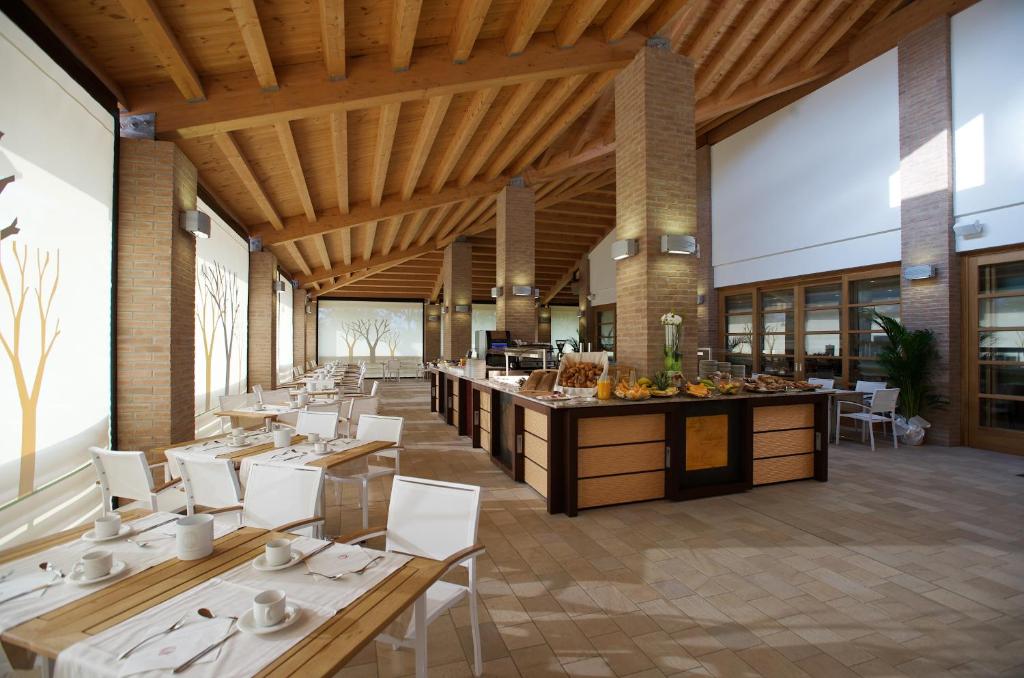 un restaurant avec des plafonds en bois et des tables et des chaises blanches dans l'établissement Green Village Eco Resort, à Lignano Sabbiadoro