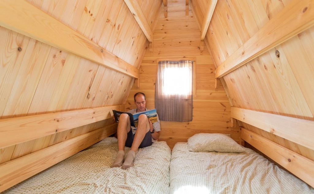 un homme assis sur un lit dans une cabane en rondins qui lit un livre dans l'établissement Ferme Rony Camp des Découvreurs, à Saint-Nizier-du-Moucherotte