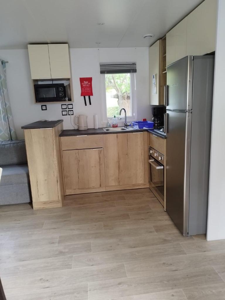 une cuisine avec des armoires en bois et un réfrigérateur en acier inoxydable dans l'établissement mobil home lac des reves, à Lattes