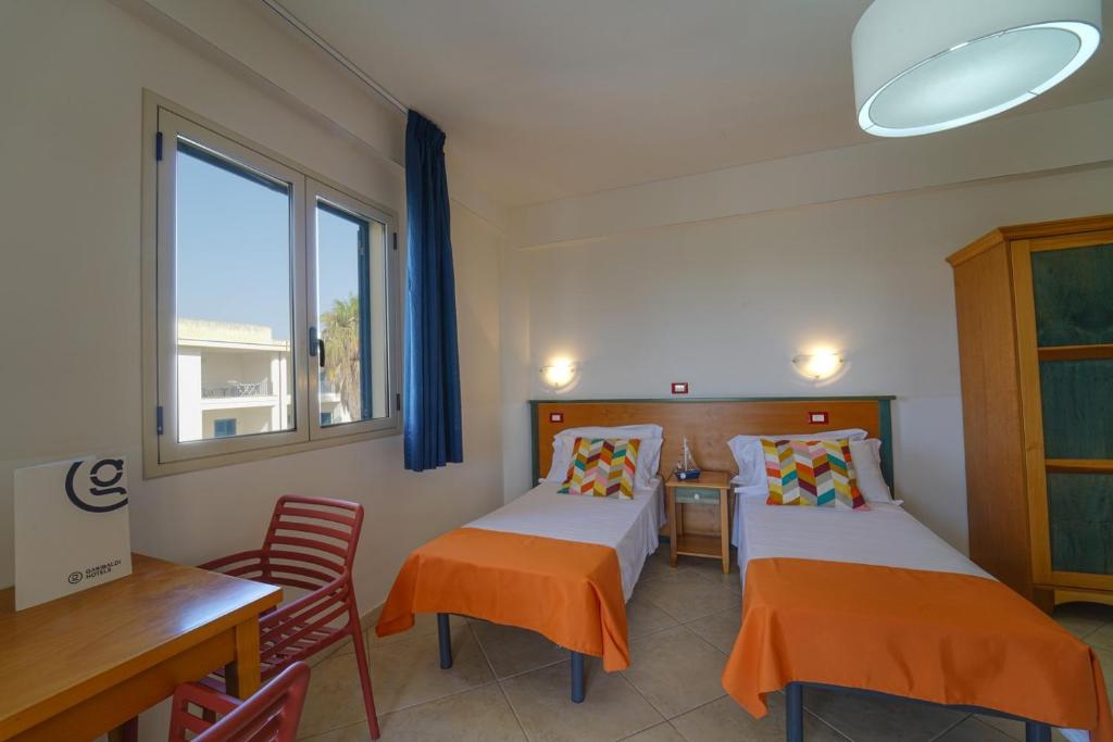 une chambre avec deux lits, une table et une fenêtre dans l'établissement GH Baraka Village, à Scoglitti