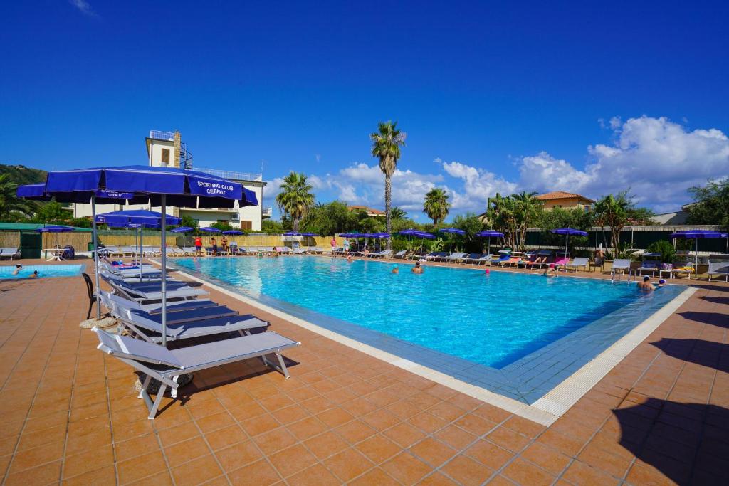 une grande piscine avec chaises longues et parasols dans l'établissement Cefalu Resort - Sporting Club, à Cefalù