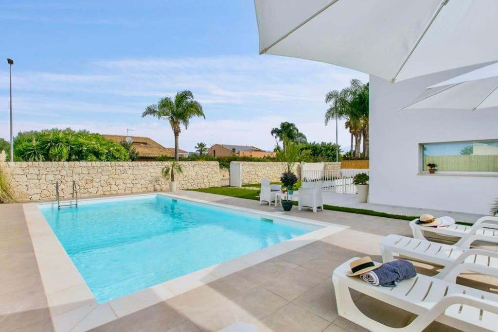 - une piscine dans une villa avec des chaises blanches dans l'établissement Domus Maulli - Villa sul mare, à Marina di Ragusa