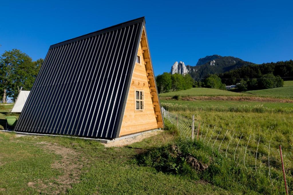 une petite maison avec un toit noir dans un champ dans l'établissement Ferme Rony Camp des Découvreurs, à Saint-Nizier-du-Moucherotte