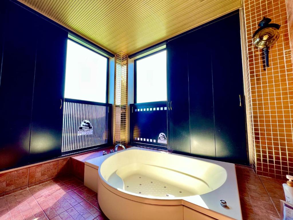 La salle de bains est pourvue d'une grande baignoire, de murs bleus et de fenêtres. dans l'établissement SKY JZauruss バズるホテル ,Dinosaur Love Hotel, à Beppu
