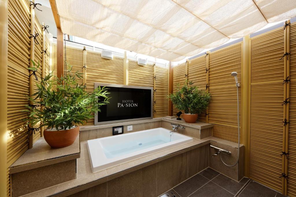 La salle de bains est pourvue d'une baignoire, d'une télévision et de plantes. dans l'établissement ホテルパシオンリゾート, à Matsuyama