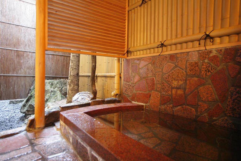 une baignoire dans une pièce avec un mur en pierre dans l'établissement Sennennoyu Koman, à Toyooka