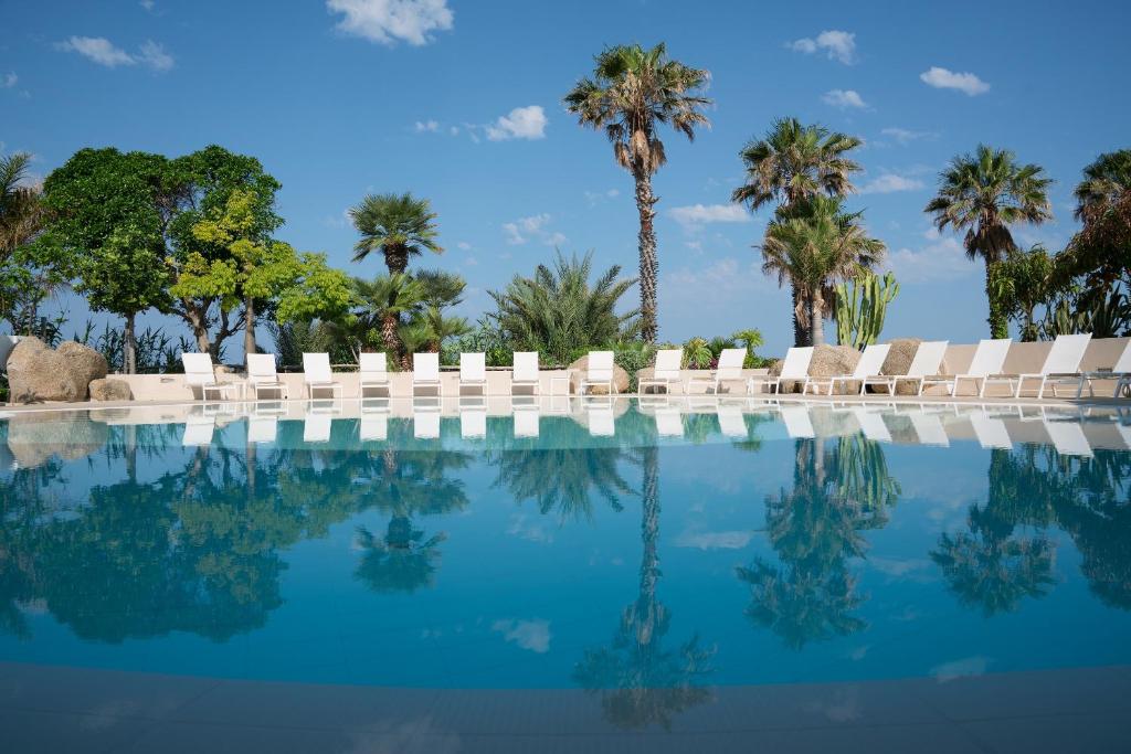une piscine avec chaises longues et palmiers dans l'établissement Hotel Villaggio Cala Di Volpe, à Capo Vaticano