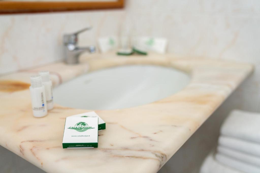 - un comptoir de salle de bains avec un lavabo et une boîte de savon dans l'établissement Hotel Villaggio Cala Di Volpe, à Capo Vaticano