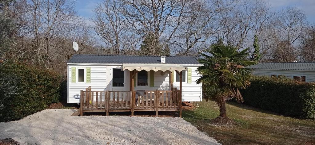 une petite maison blanche avec une véranda et un arbre dans l'établissement CAMPING LE BEL AIR Mobil home L'OLIVIER 4 personnes, à Limogne-en-Quercy