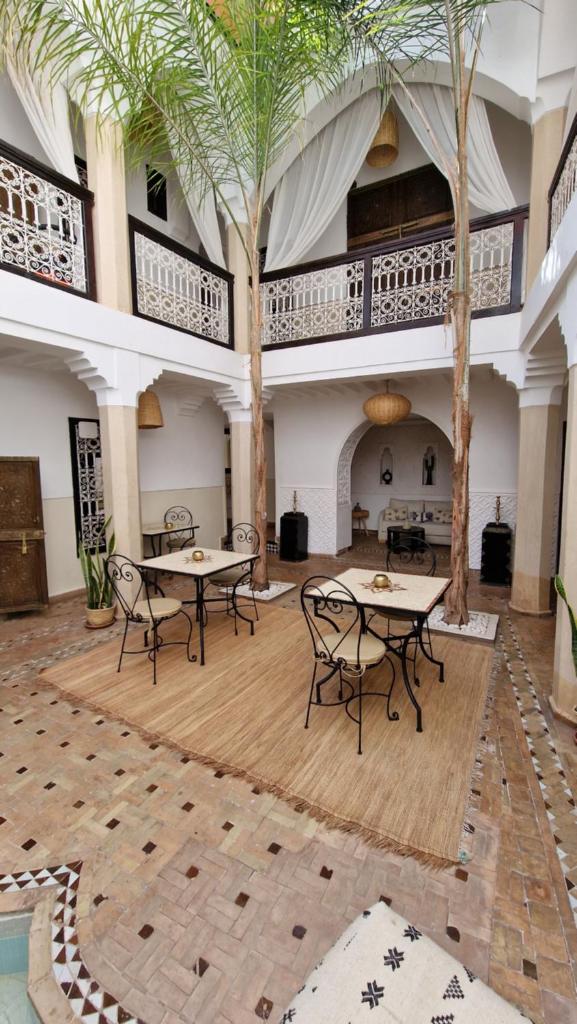 une chambre avec des tables, des chaises et des palmiers dans l'établissement Riad Des Arts, à Marrakech