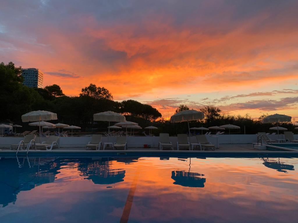 - un coucher de soleil au-dessus d'une piscine avec chaises longues et parasols dans l'établissement Hotel Beau Rivage Pineta, à Lido di Jesolo