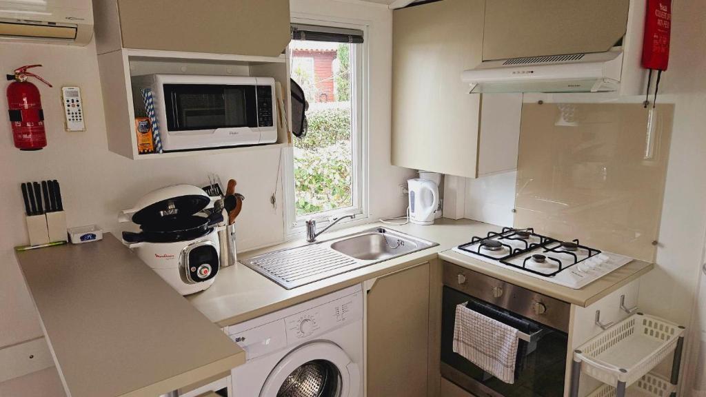une petite cuisine avec un évier et une machine à laver dans l'établissement Joli Mobil home N°11, 4ch tout confort et spacieux, à Gastes