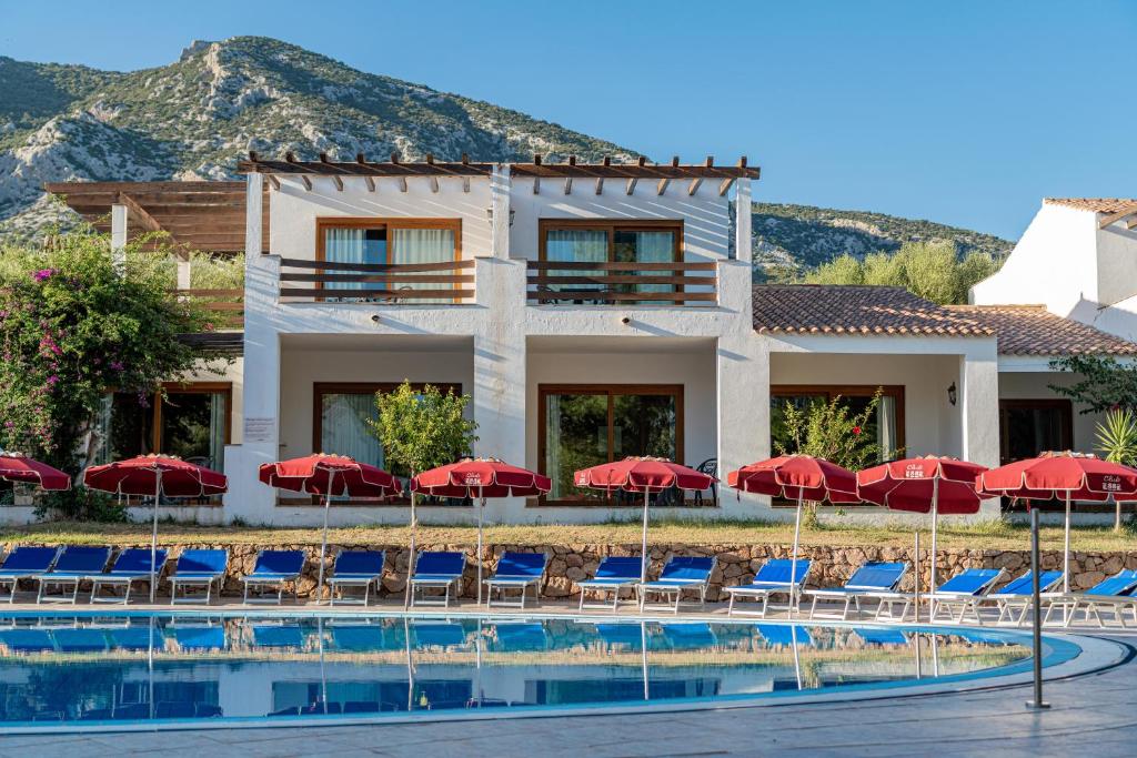 un complexe doté d'une piscine avec des chaises longues et des parasols rouges dans l'établissement Club Esse Palmasera, à Cala Gonone