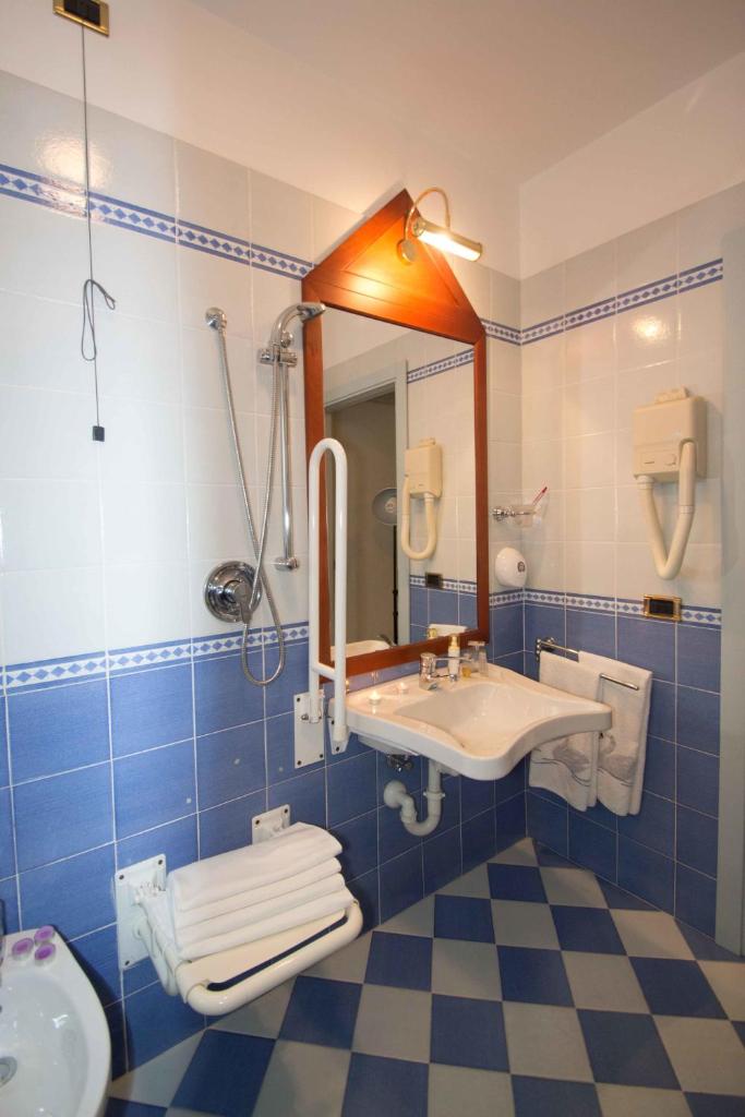 La salle de bains est pourvue de carrelage bleu, d'un lavabo et d'un miroir. dans l'établissement Hotel Costazzurra, à Grottammare