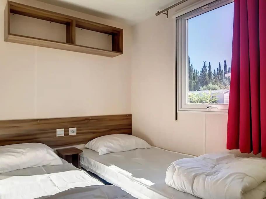 - 2 lits dans une chambre avec fenêtre et rideaux rouges dans l'établissement Le Moorea Mobilhome Camping le Montourey 4 étoiles, à Fréjus