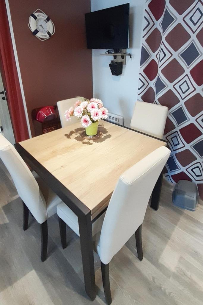 une table en bois avec des chaises blanches et un vase de fleurs. dans l'établissement MH 127 Bois Dormant 3ch climatisé, à Saint-Jean-de-Monts