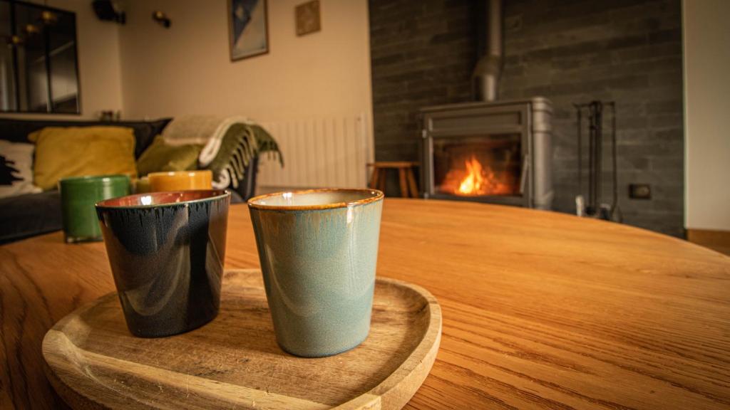 2 tasses assises sur une table en bois avec une cheminée dans l'établissement Chalet Peak Noir entier 12pers - Cosy House Peak Noir for 12people, au Monêtier-les-Bains