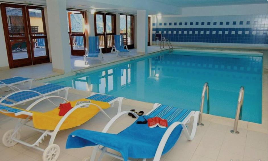 une grande piscine avec de l'eau bleue et des chaises bleues dans l'établissement Appartement 6 couchages au pied des pistes à Orcières 2 chambres, balcon et parking couvert, à Orcières