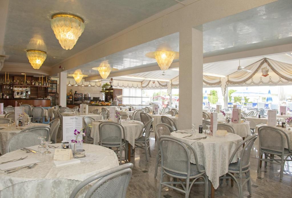 un restaurant avec des tables et des chaises blanches et des lustres dans l'établissement Hotel Panama, à Lido di Jesolo
