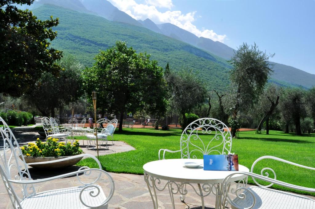 une table et des chaises dans un parc avec des montagnes en arrière-plan dans l'établissement Club Hotel Olivi - Tennis Center, à Malcesine