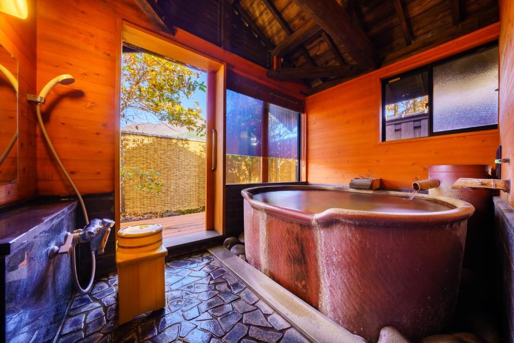 La grande salle de bains en bois est pourvue d'une baignoire et d'une fenêtre. dans l'établissement 由布の里 旅荘 牧場の家 Ryoso Makibanoie, à Yufu