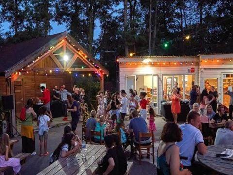 une foule assise autour d'une fête devant deux remorques dans l'établissement Camping Marvilla Parks -Parc des roches 91530, à Saint-Chéron