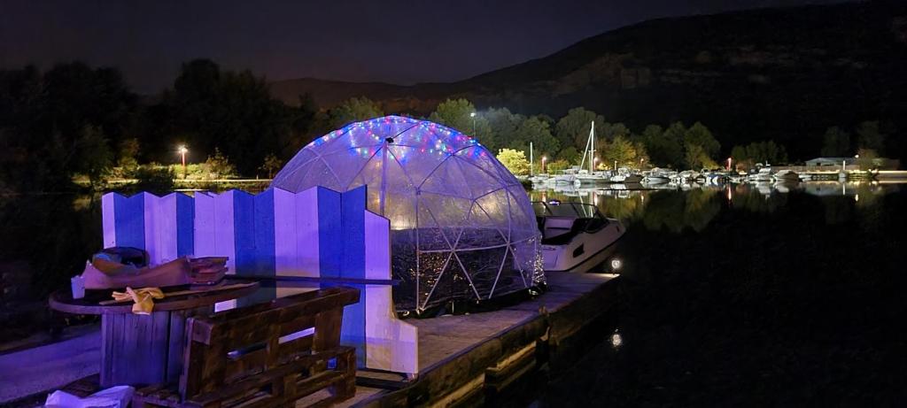 une personne assise dans un kiosque sur l'eau la nuit dans l'établissement Eden marine, à Montalieu-Vercieu