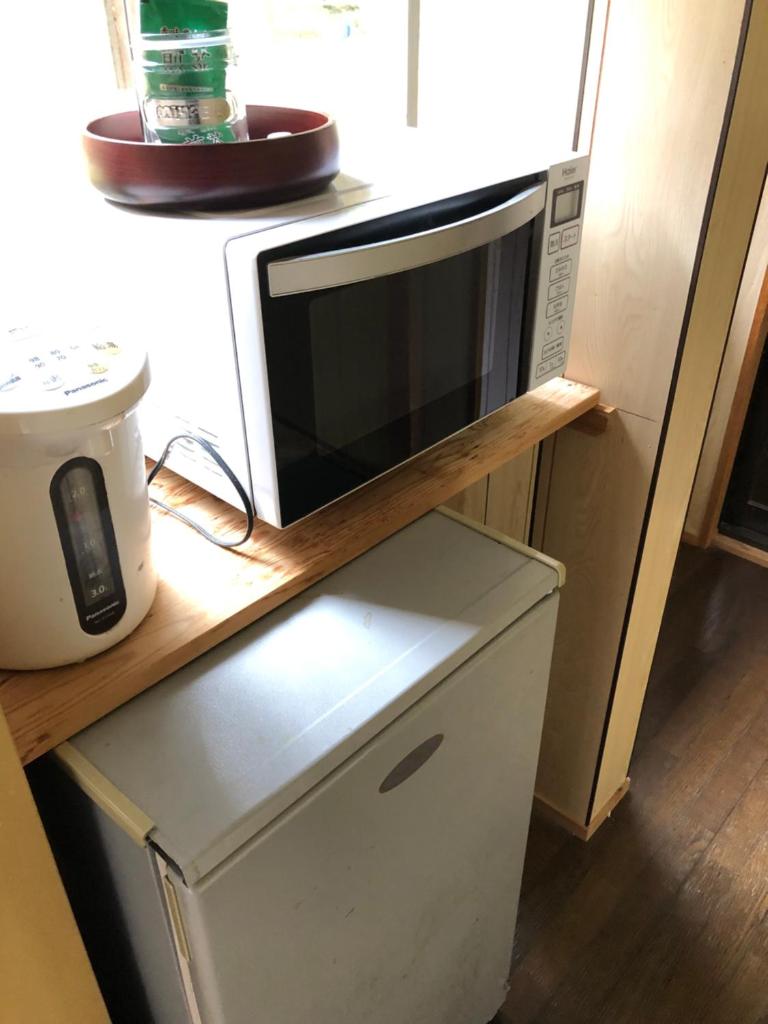 Un four micro-ondes est installé au-dessus d'une étagère en bois. dans l'établissement Minshuku Kawarabi-so, à Nosegawa