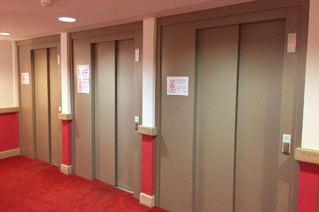 une rangée de portes d'ascenseur dans une chambre avec moquette rouge dans l'établissement RisoulSki Antarès - Piscine et Sauna, à Risoul