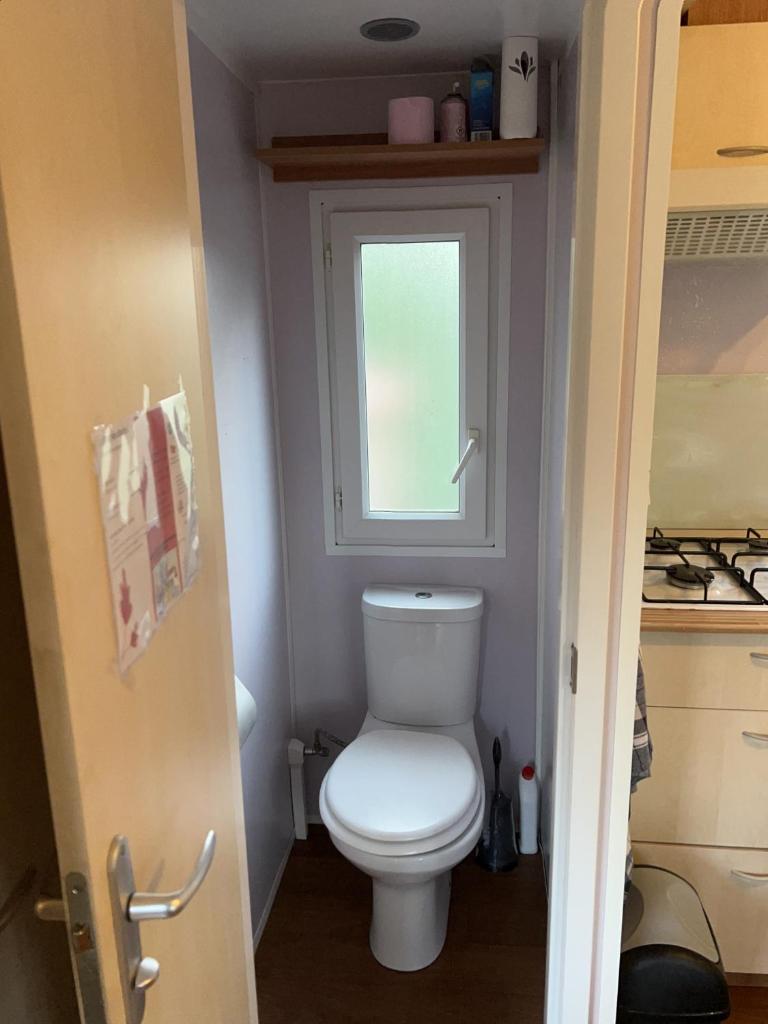 Elle comprend une petite salle de bains pourvue de toilettes et d'une fenêtre. dans l'établissement mobil home, à Mirgaudon