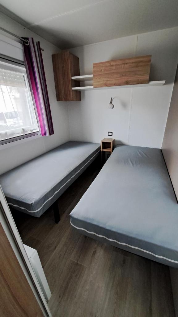 une petite chambre avec deux lits et une fenêtre dans l'établissement Mobile Home Climatisé 3 chambres à Narbonne Plage, à Narbonne-Plage