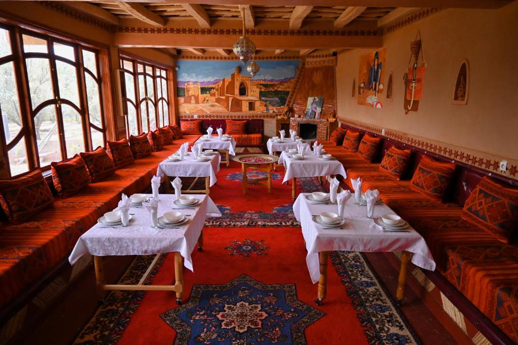 une salle à manger avec des tables et des chaises blanches et des fenêtres dans l'établissement kasbah amlal, à Boumalne