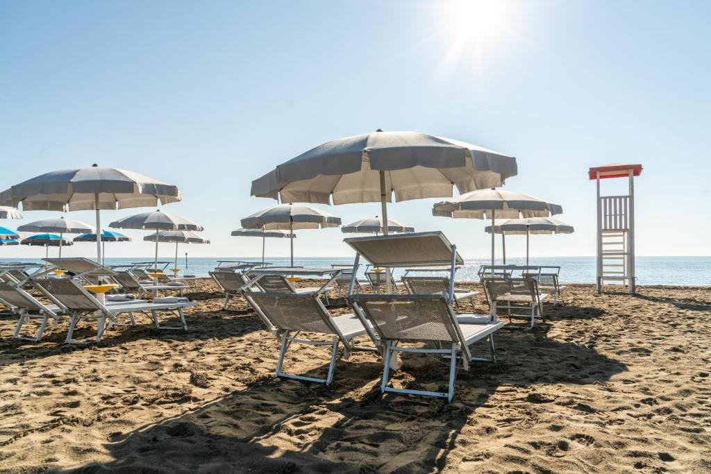 un groupe de chaises et de parasols sur une plage dans l'établissement Hotel Athena, à Lignano Sabbiadoro