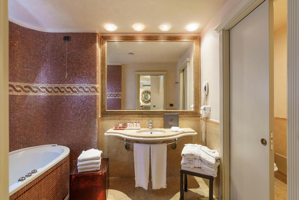 une salle de bain avec un lavabo, une baignoire et un miroir dans l'établissement Romano Palace Luxury Hotel, à Catane