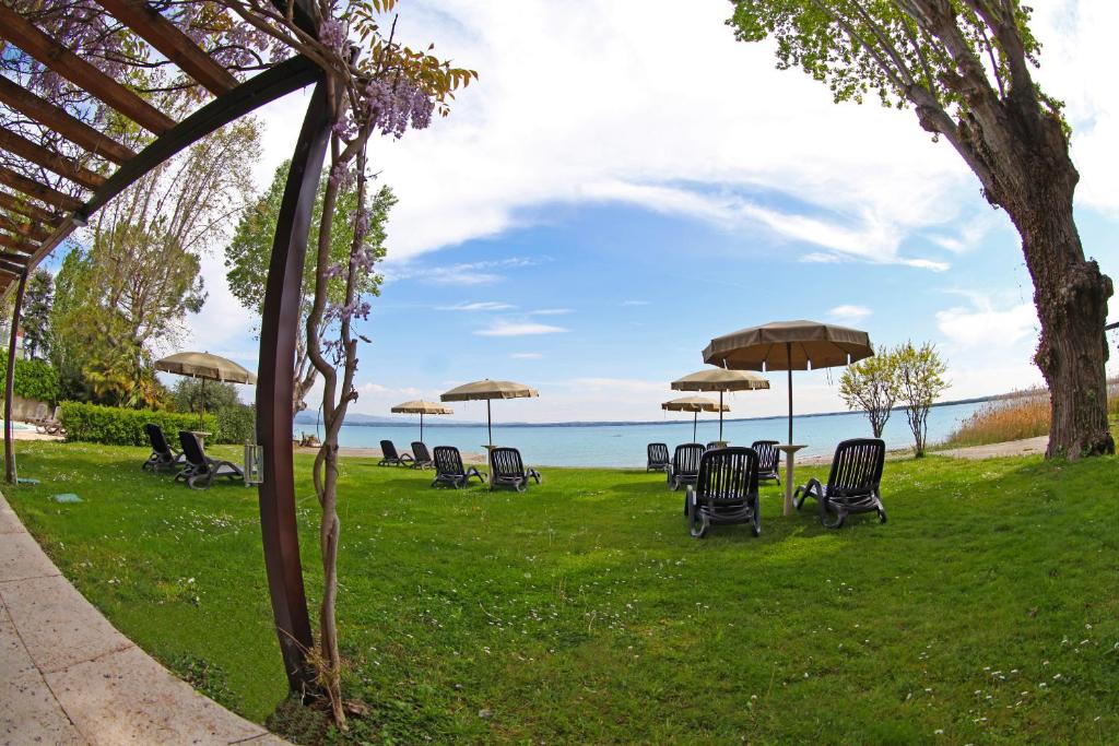 un groupe de chaises et de tables avec des parasols sur l'herbe dans l'établissement Hotel Smeraldo, à Sirmione