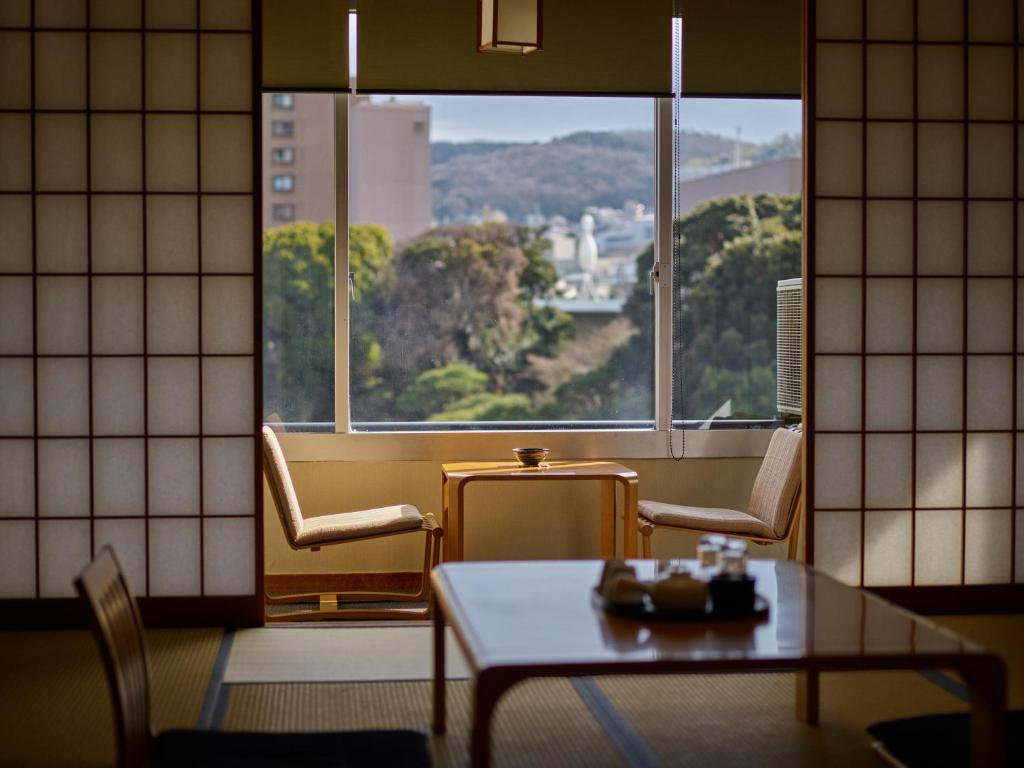 une pièce avec une table et une grande fenêtre dans l'établissement Ito Yukitei, à Itō