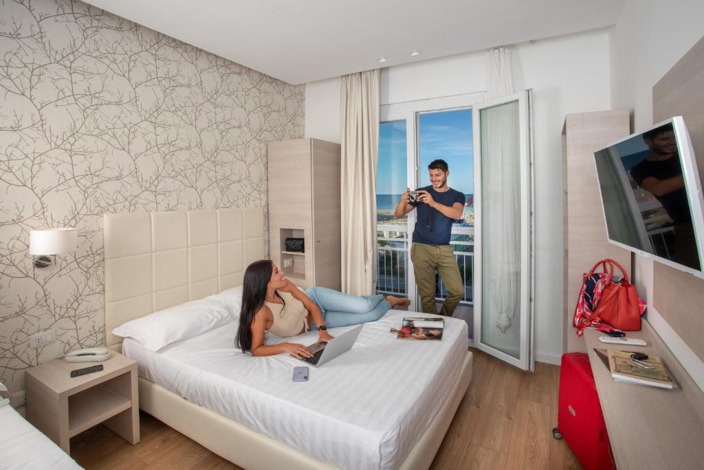 une femme assise sur un lit dans une pièce avec un ordinateur portable dans l'établissement Hb Hotels Orchidea Blu, à Rimini