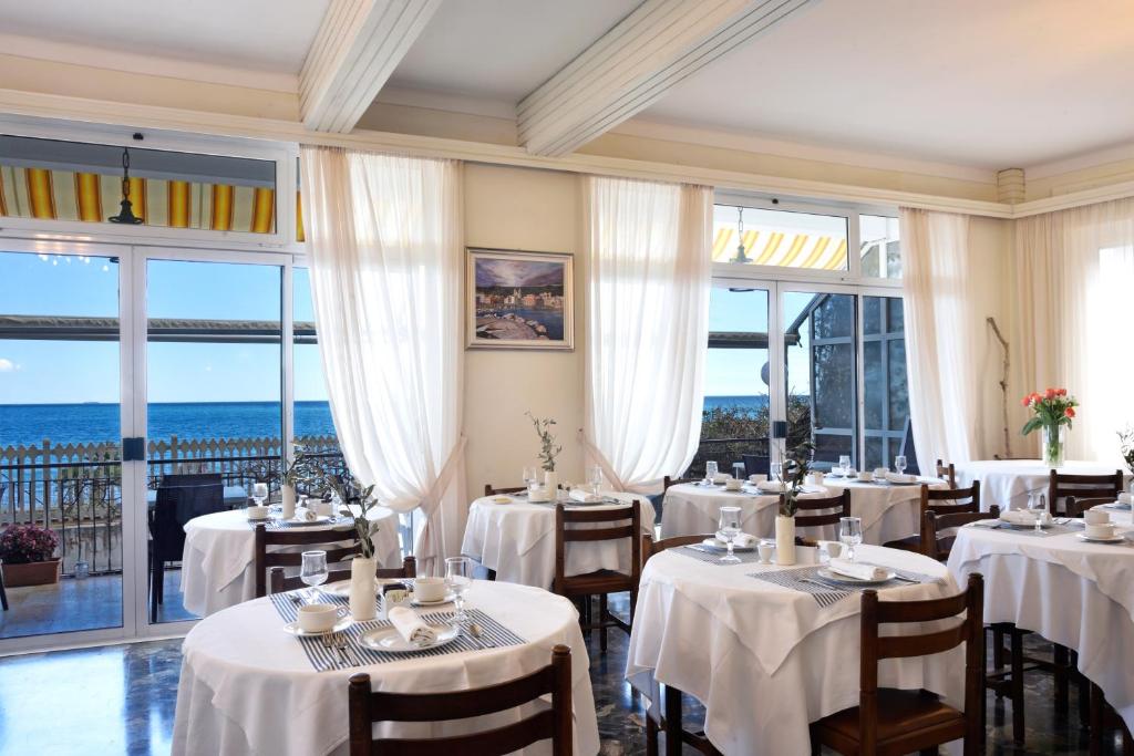 un restaurant avec des tables et des chaises blanches et des fenêtres dans l'établissement Hotel Villa Giulia, à Laigueglia