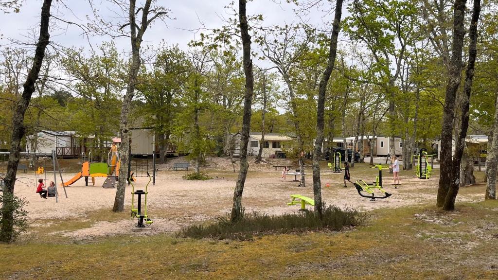 un parc avec une aire de jeux avec des balançoires et des arbres dans l'établissement Le charme du Bassin d Arcachon en Mobil Home climatisé, à Arès