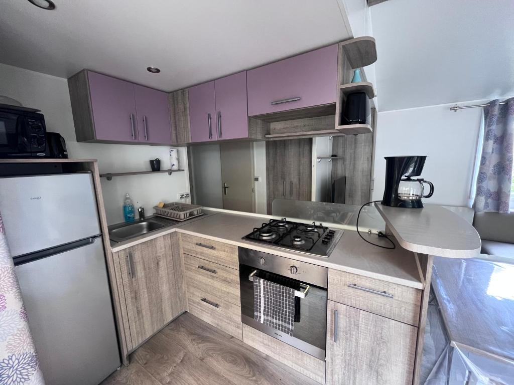 - une petite cuisine avec des placards violets et une cuisinière dans l'établissement Camping Marvilla Parks - Rivages des Landes - Mobil home 3 chambres, à Aureilhan 1 autre photo
