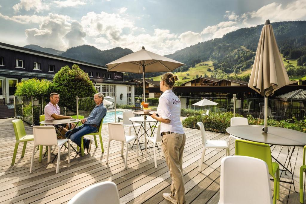 une femme debout sur une terrasse avec des gens assis à des tables dans l'établissement Belambra Clubs Praz-sur-Arly - L'Alisier, à Praz-sur-Arly