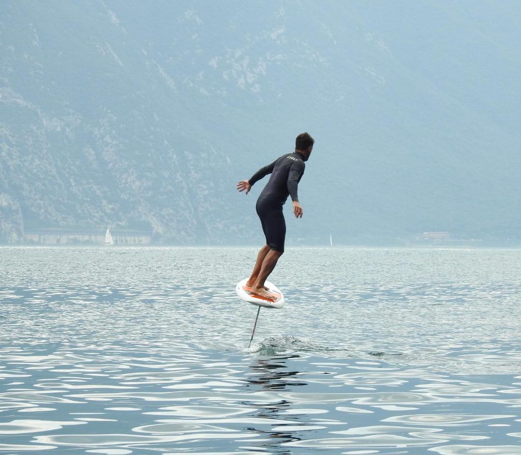 un homme en combinaison de plongée sur une planche de surf dans l'eau dans l'établissement Surf Hotel Pier - Montagnoli Group, à Limone sul Garda