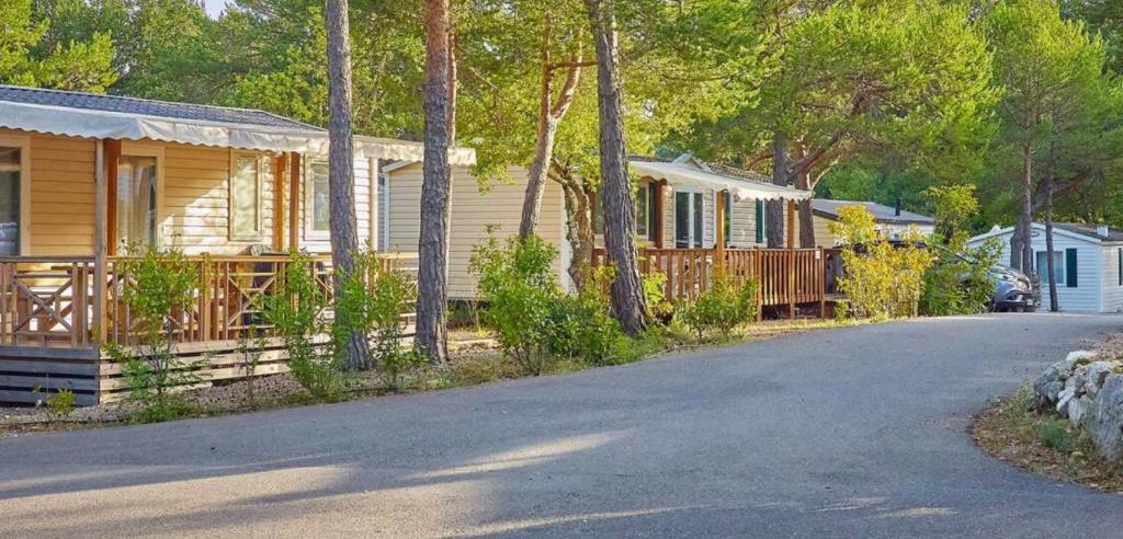 une rangée de chalets à côté d'une route avec une maison dans l'établissement Mobil-home dans camping 4*, à Saint-Laurent-du-Verdon