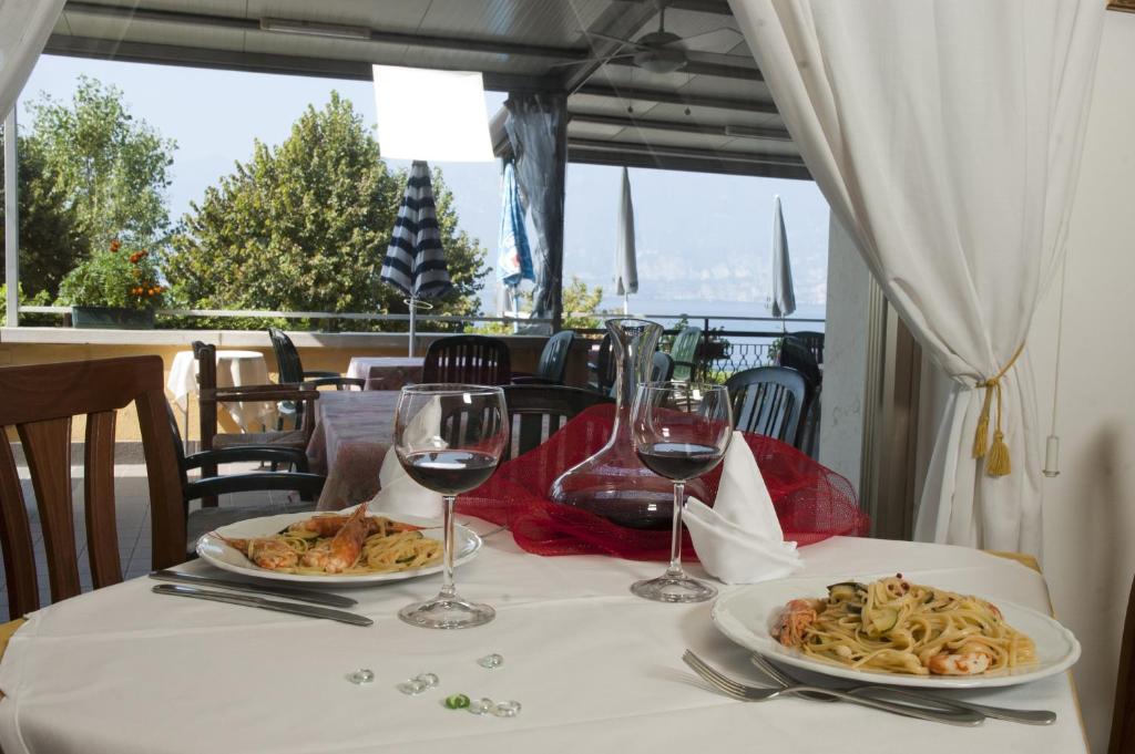- une table avec deux assiettes de nourriture et des verres à vin dans l'établissement Hotel Merano, à Brenzone